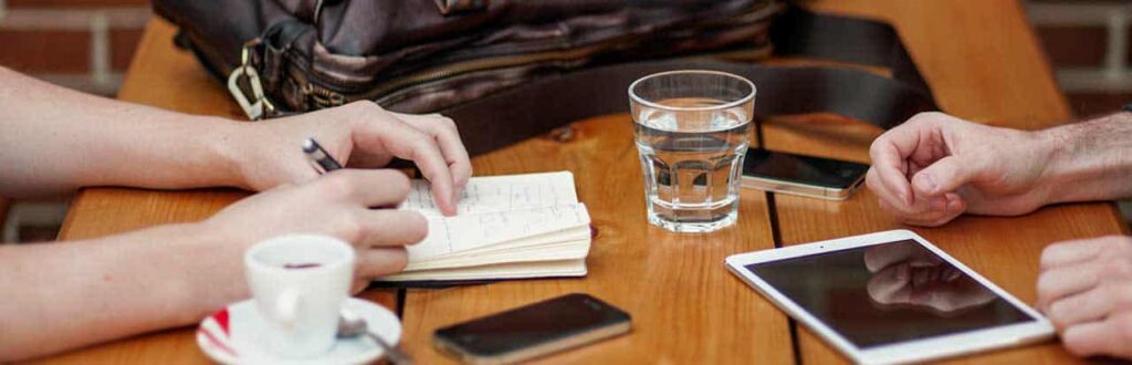 Empower Employees With A Wiki - People across the table from each other with a tablet and cell phone on table