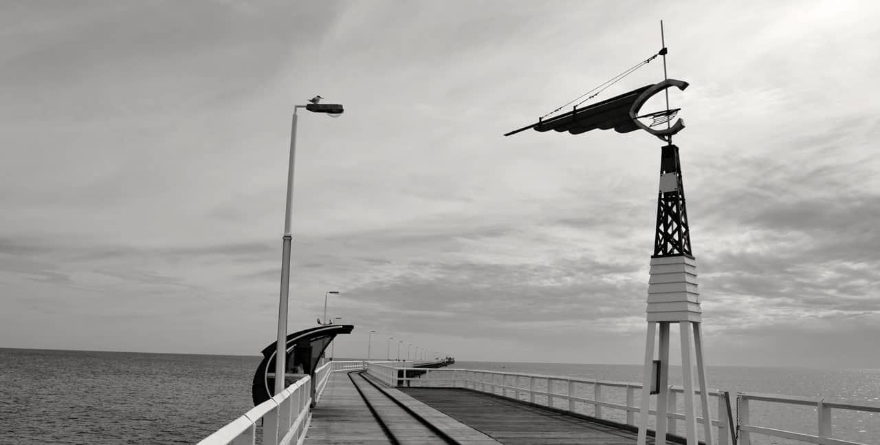 Long pier on ocean with railroad track on it.